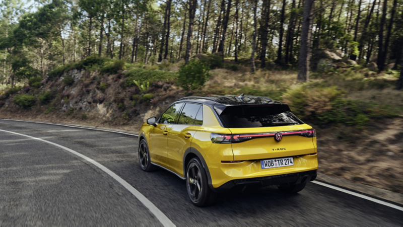 En gul T-Roc sedd snett bakifrån körandes längs en väg kantad av skog