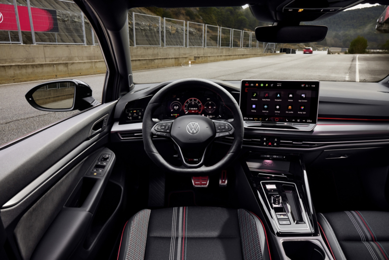 Rear view of a red VW Golf GTI in front of a shop. A man and a woman with snacks in hand approach you.