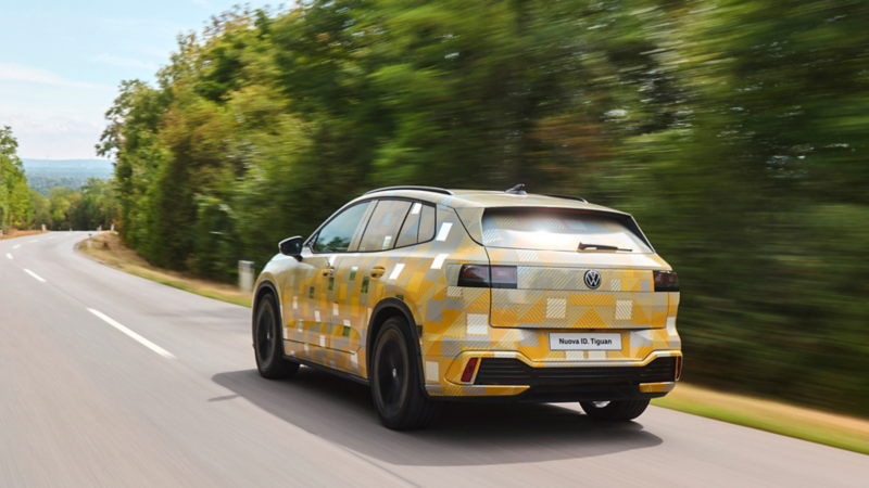 Vista posteriore di una ID. Tiguan con carrozzeria camouflage che percorre una strada di campagna.