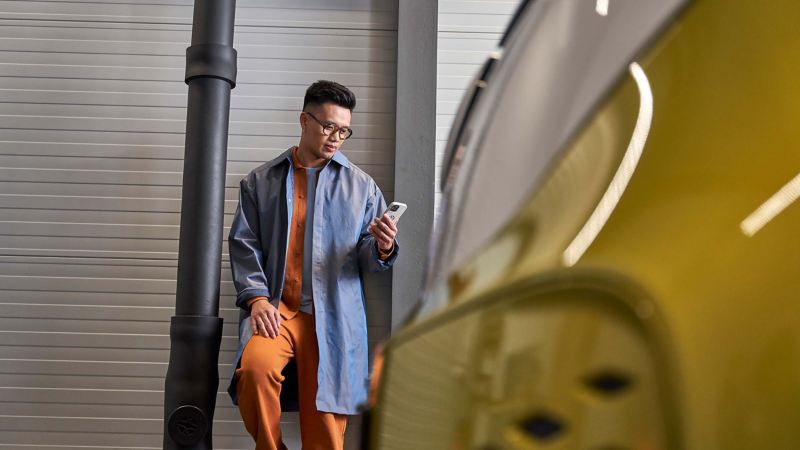 A man stood infront of a parked ID. Buzz looking at his smartphone. 