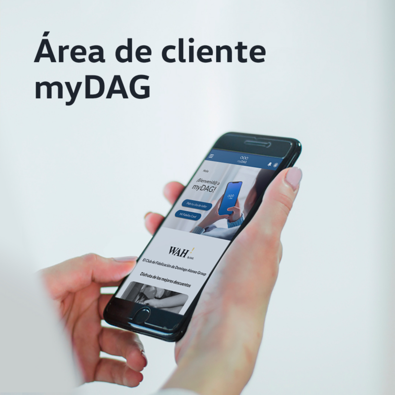 Manos sosteniendo un smartphone que muestra la aplicación móvil 'myDAG', el club de fidelización de Domingo Alonso Group. En la pantalla se ve el logo 'WAH' y la frase 'Disfruta de las mejores descuentos', indicando acceso a beneficios y un programa de fidelidad.