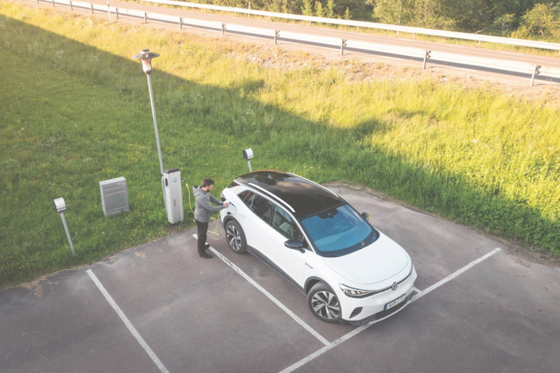Vit Volkswagen ID. 4 laddas vid en publik laddstation på landsbygden, sedd uppifrån