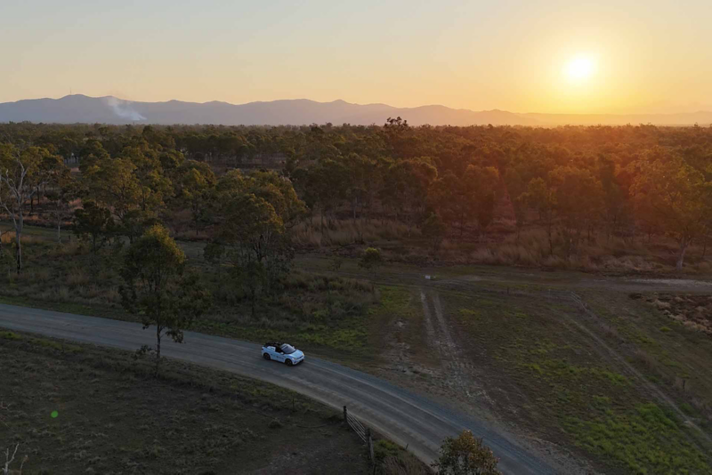 Aerial shot of ID.4 driving at sunset with rainforest and mountains in the background
