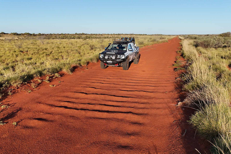 Amarok driving through red desert road with shrubs either side