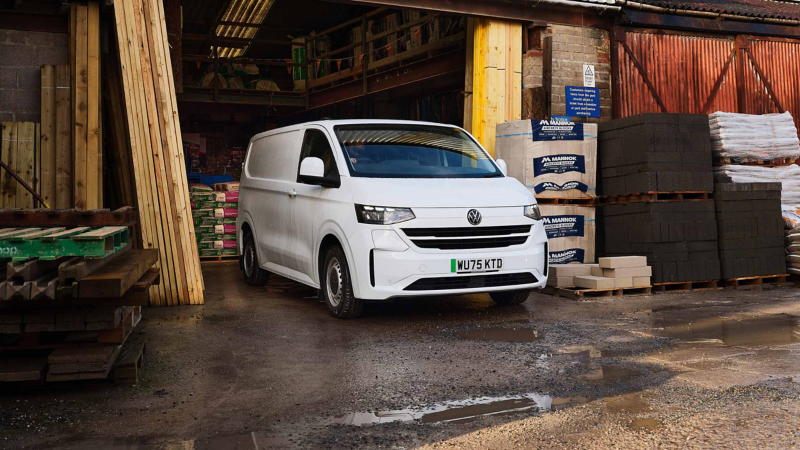 A white Volkswagen van parked in a warehouse entrance. Surrounding are stacks of building materials and wooden planks, conveying a worksite atmosphere.