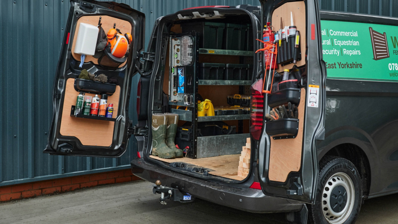 A van with rear doors open, revealing organized tools and equipment. Shelves hold boots, cleaning supplies, and tools, conveying a tidy, professional tone.