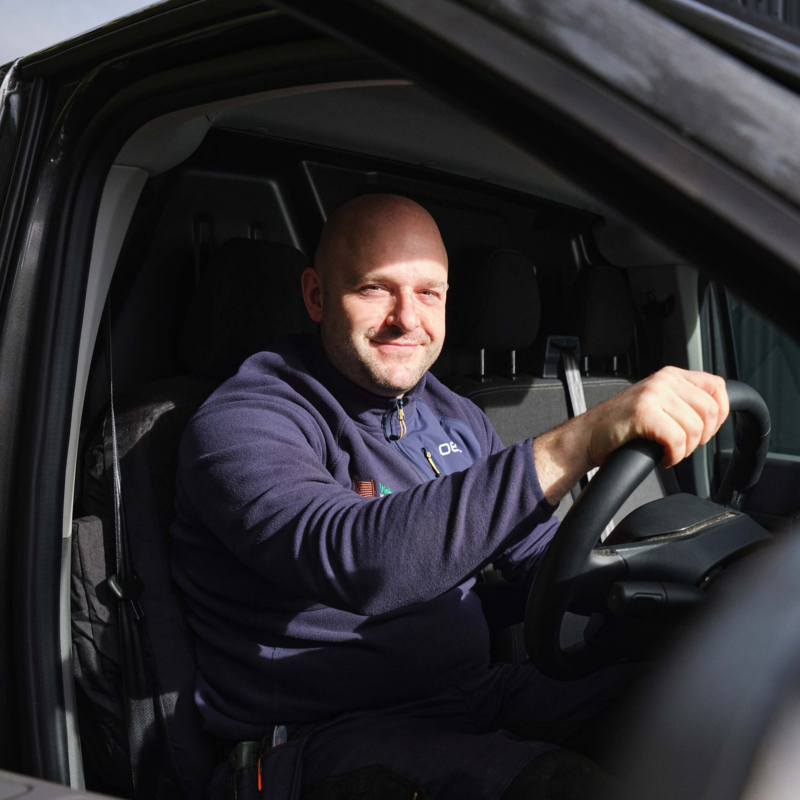 Chris Welbourne sit in the driving seat and holding the steering wheel of a Volkswagen e-Transporter Panel Van