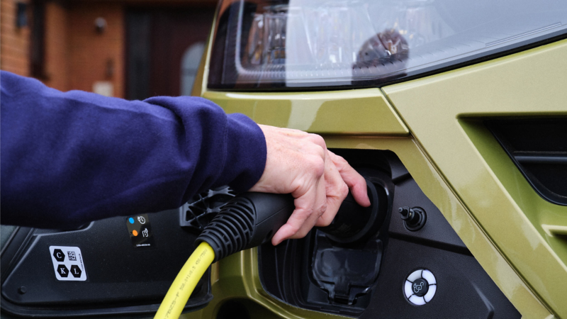 A person plugging a charging cable into a green e-Transporter Kombi
