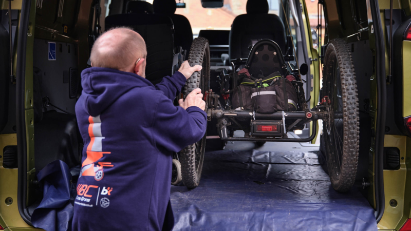 A man loading the opened booth of an e‑Transporter Kombi with a handcycle