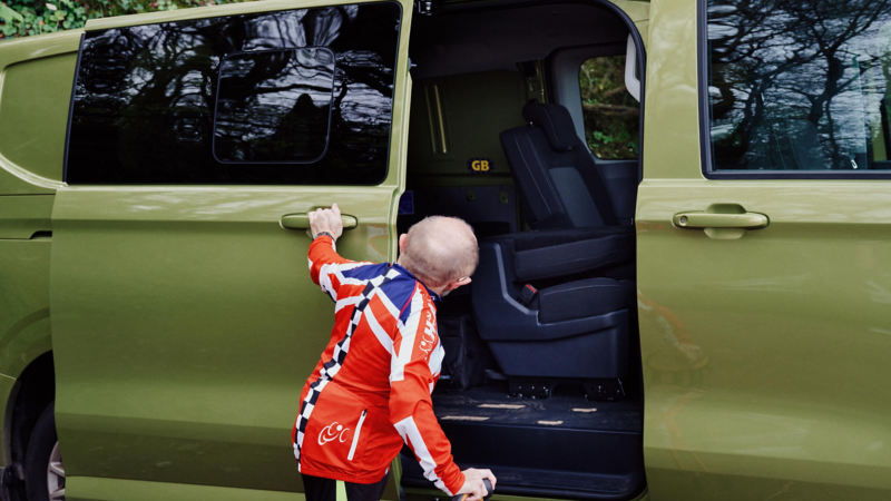 A man closing the sliding door of a green e-Transporter Kombi van