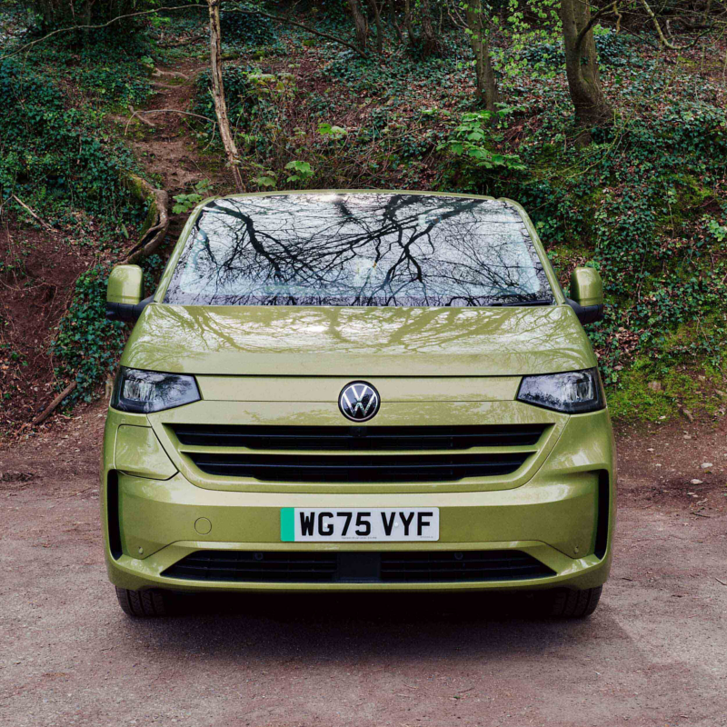 Front-facing VW e‑Transporter Kombi in green parked in a rural area