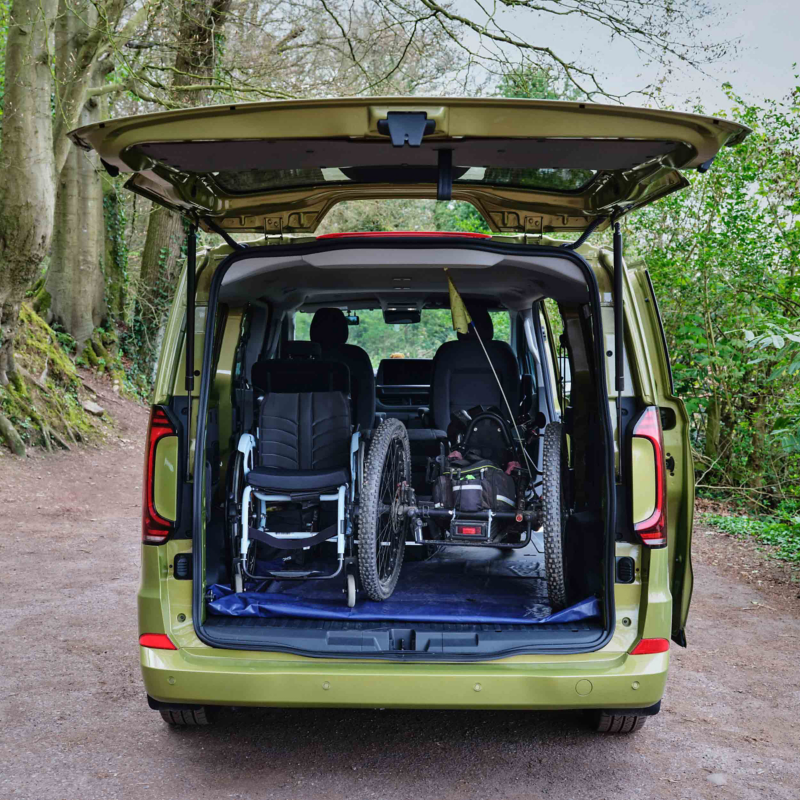 Rear view of an electric VW e-Transporter Kombi van with an opened booth showing a wheelchair and handcycle loaded inside