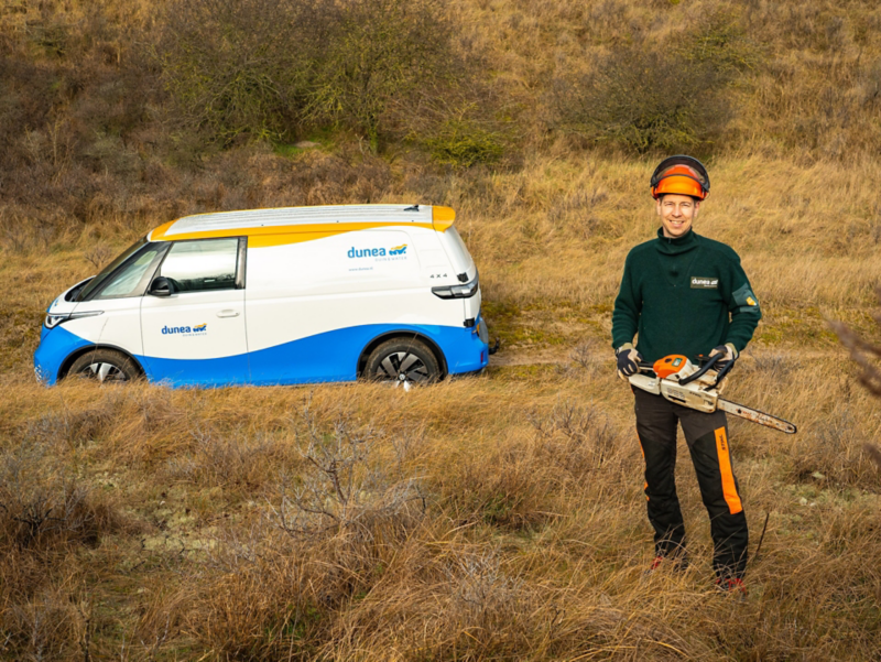 Zijkant van de ID. Buzz Cargo van Dunea met vakman met kettingzaag in de hand