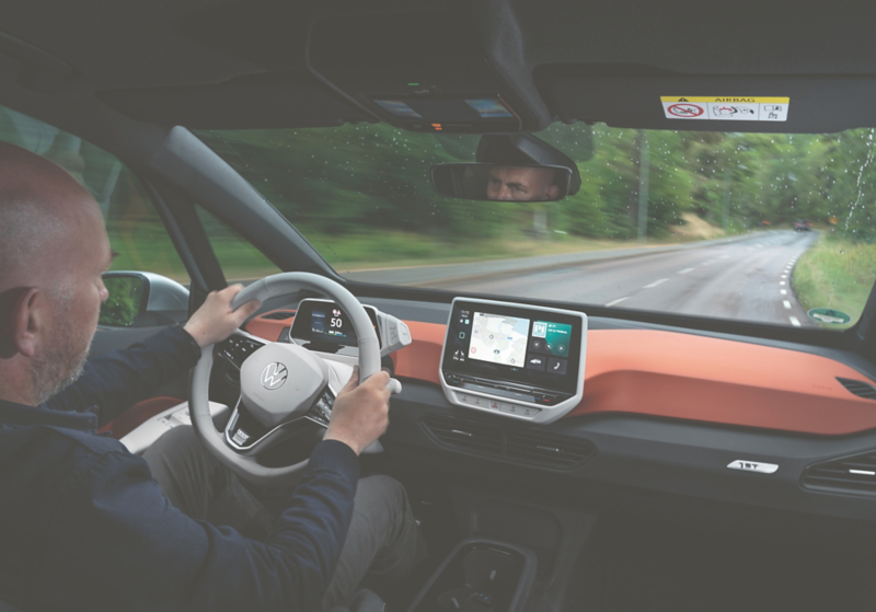 Interiörbild där en förare kör en Volkswagen ID.3 på landsväg, med instrumentpanel och infotainmentskärm i fokus