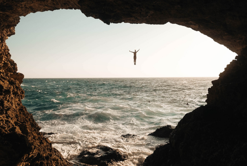 Pauline Ollén mitt i ett hopp från en klippa, fotad från en grotta.
