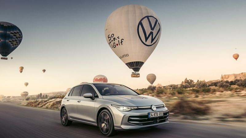 a new silver Golf driving in the desert with a hot air balloon in the background