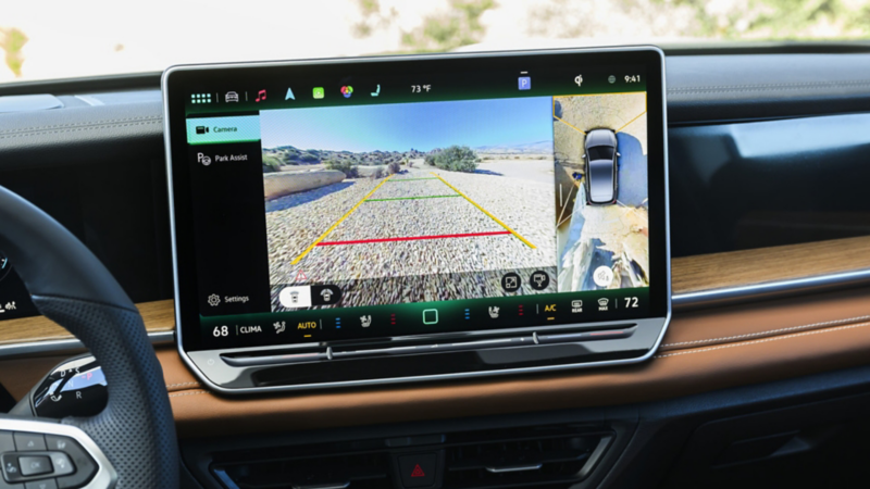 In-car touchscreen display showing a rear-view camera with parking assist guidelines and a split-screen view, highlighting modern driver-assistance technology.