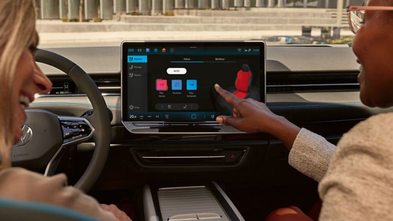 a passenger pointing to the screen in a Volkswagen car demonstrating how the climate control feature works
