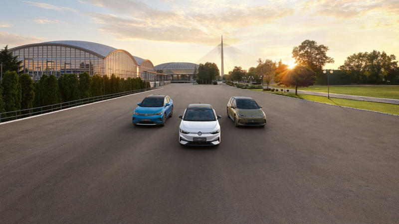 Ein roter VW Golf GTI EDITION 50 fährt im Sonnenaufgang auf einer Straße durch die Landschaft. Ebenfalls abgebildet ist das Logo des Goldenen Lenkrads 2025.