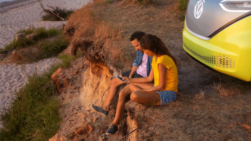 A couple sitting on the edge of a cliff behind their vehicle