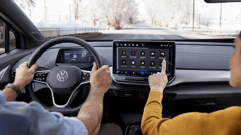 Interior of a Volkswagen ID.4 with driver and passenger using the touchscreen while driving on a snowy road.