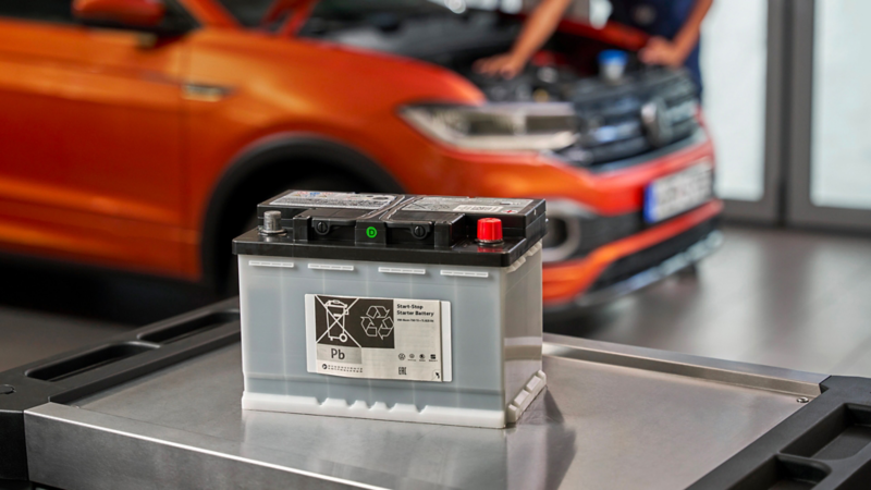 Volkswagen Genuine EFB/EFB+ Starter Battery on a roller container, a VW T-Cross in the background