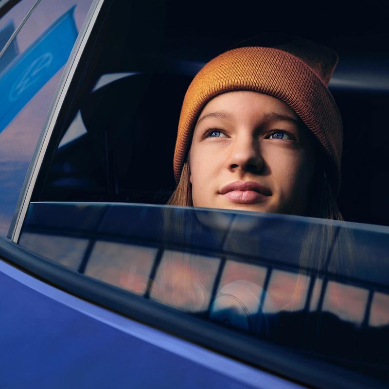 Eine junge Frau schaut verträumt aus dem offenen Fenster eines Autos in den Himmel