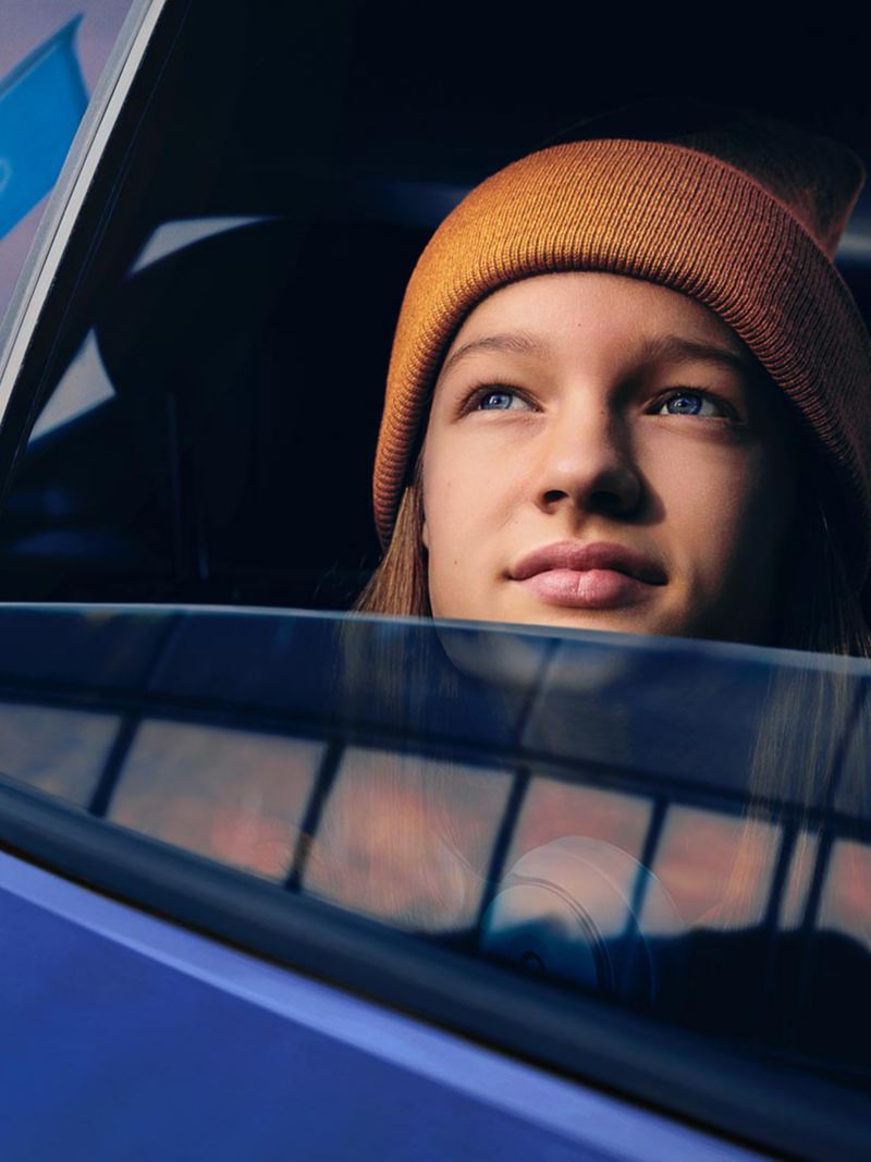 Eine junge Frau schaut verträumt aus dem offenen Fenster eines Autos in den Himmel.
