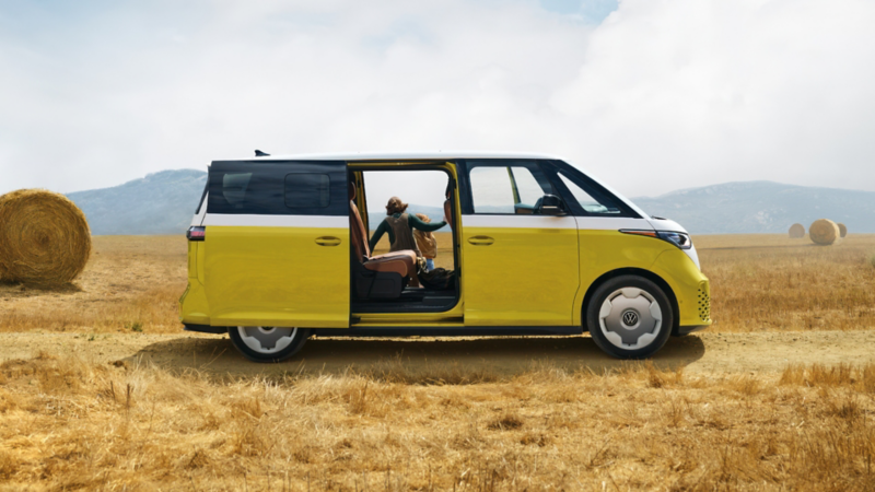 Fourgon jaune vif stationné dans un champ doré avec des balles de foin, porte latérale ouverte tandis qu’une personne se détend à l’intérieur, évoquant un style de vie aventureux et la liberté de voyager.