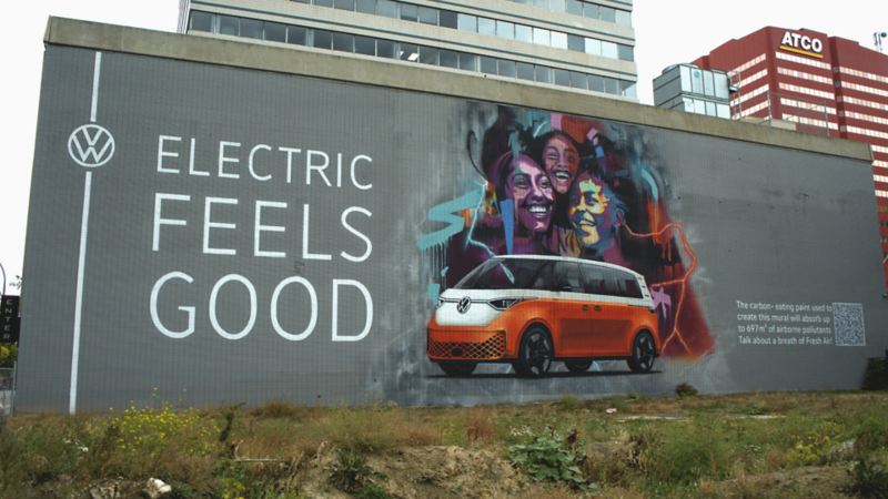 A mural on a building depicts an orange Volkswagen ID. Buzz with the tagline "ELECTRIC FEELS GOOD."