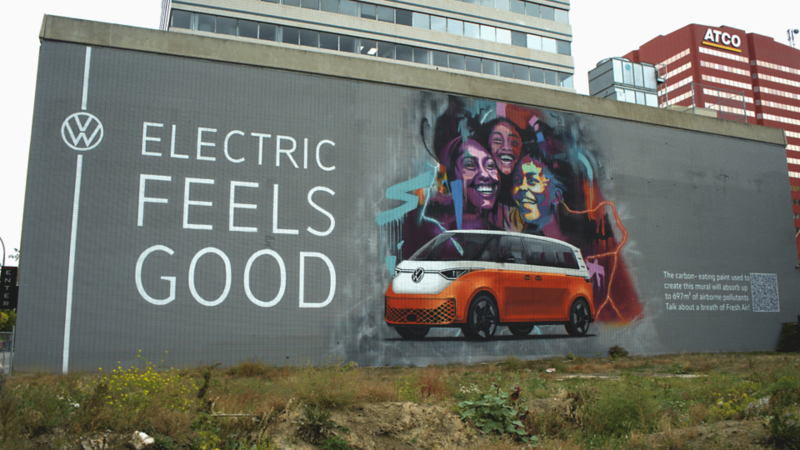 Une fresque sur un bâtiment présente un Volkswagen ID. Buzz orange avec le slogan "ELECTRIC FEELS GOOD".