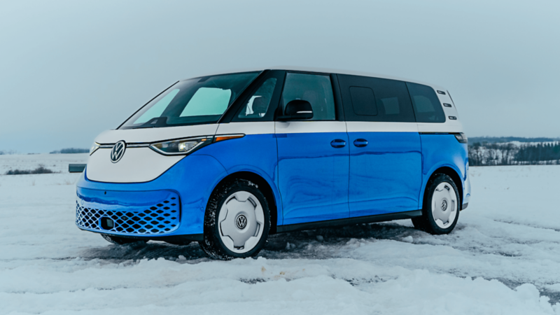 A blue and white two-tone Volkswagen ID. Buzz van parked on a snowy road with a winter landscape in the background.
