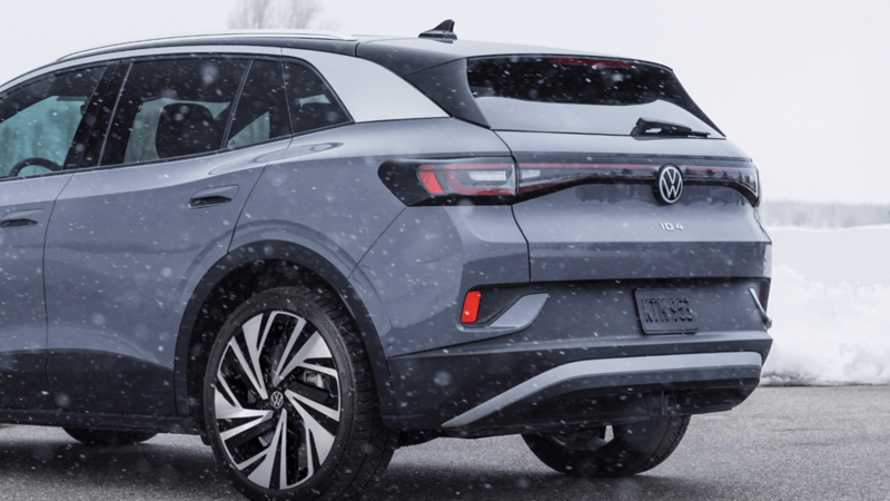 Rear three-quarter view of a grey Volkswagen ID.4 SUV driving in snowy conditions, showing the taillights and wheels.