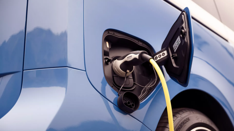 Close-up of a blue electric vehicle's charging port with a yellow charging cable securely plugged in.