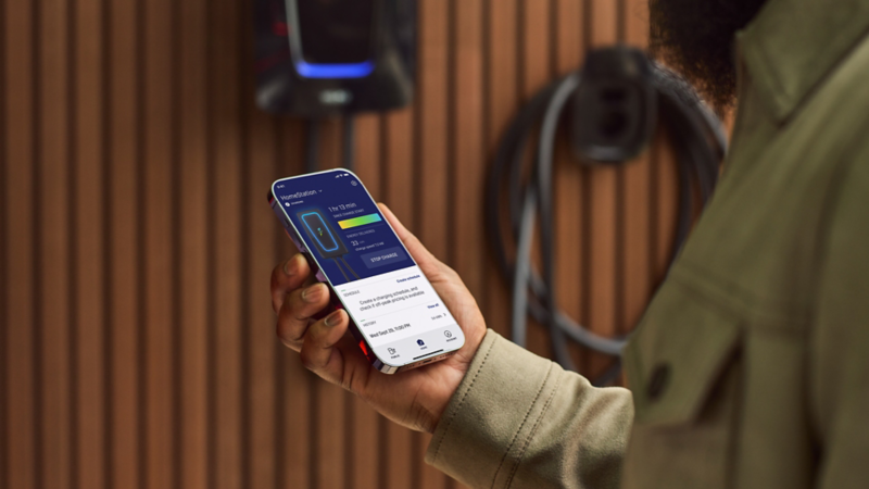 Un homme utilise une application pour smartphone pour surveiller la progression de la charge d'un véhicule électrique branché à une borne de recharge.