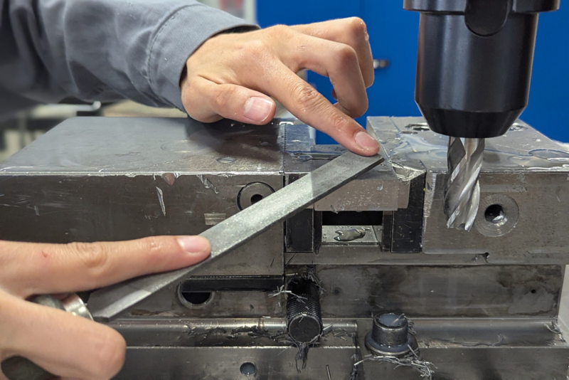 Nahaufnahme einer Maschine und von zwei Händen, die ein Metallstück feilen