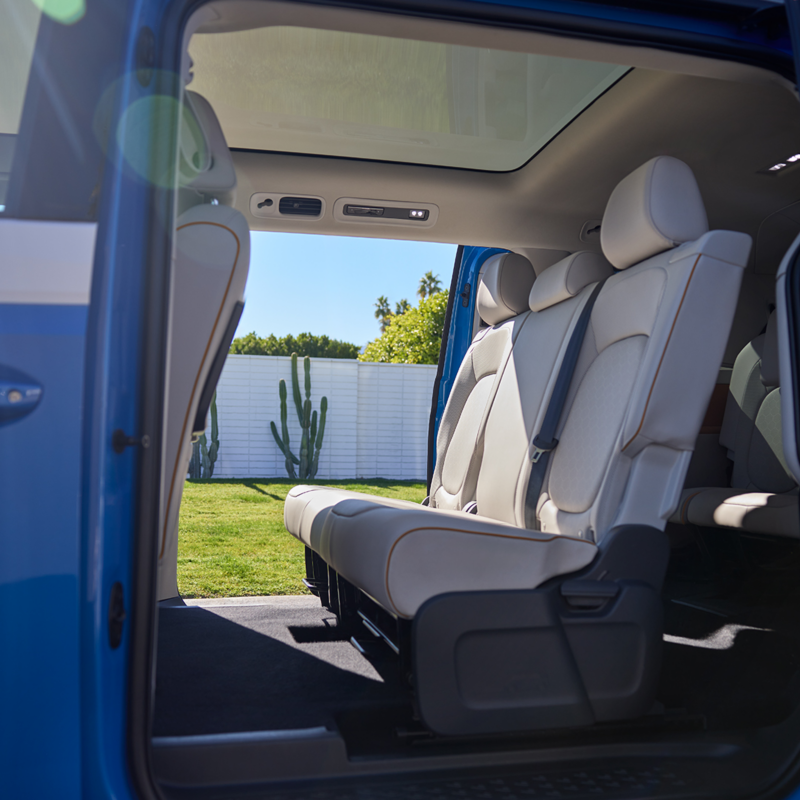 L'intérieur spacieux du Volkswagen ID. Buzz 2025 avec sièges spacieux, toit panoramique et portes coulissantes ouvertes avec la pédale virtuelle "Easy Open". 