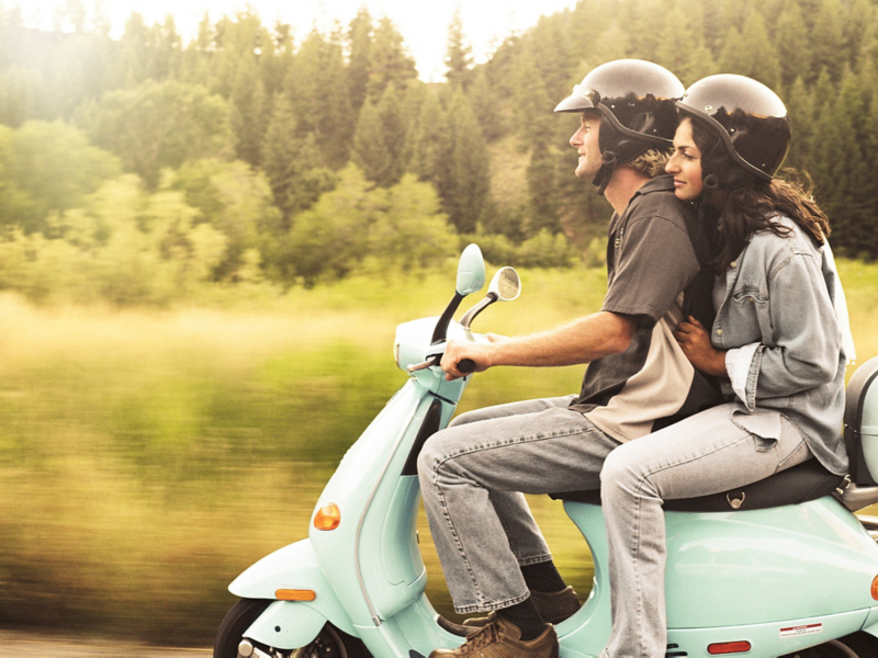 Young people riding on an electric scooter side view