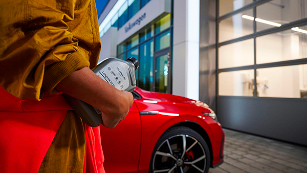 Inquadratura di una persona reggere in mano una bottiglia di olio per motore LongLife III FE e sullo sfondo un veicolo Volkswagen. 
