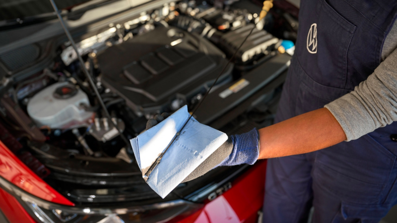 Inquadratura di un meccanico Volkswagen controllare il livello dell'olio della vettura.