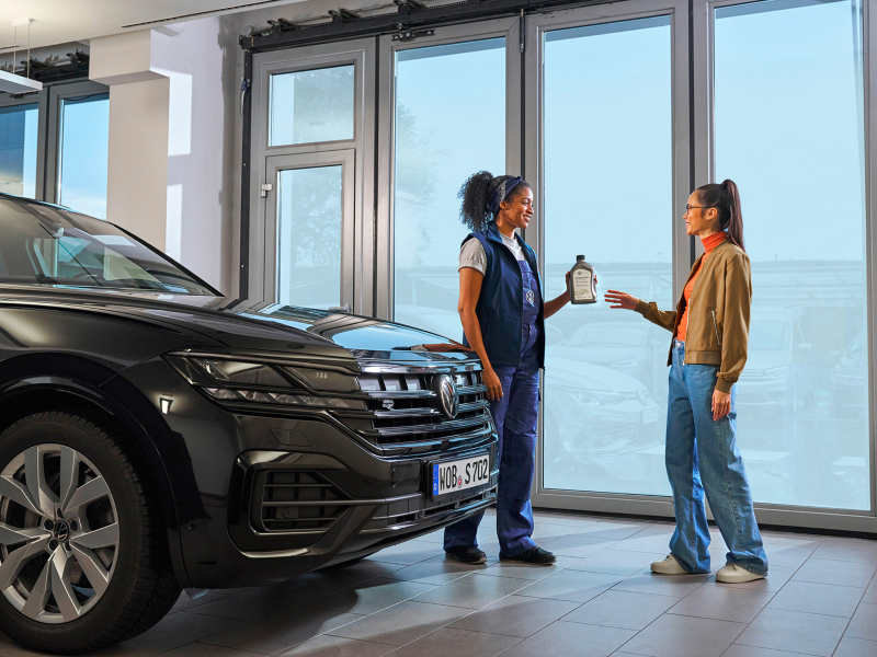 VW service employee hands customer a bottle of engine oil next to a VW Touareg