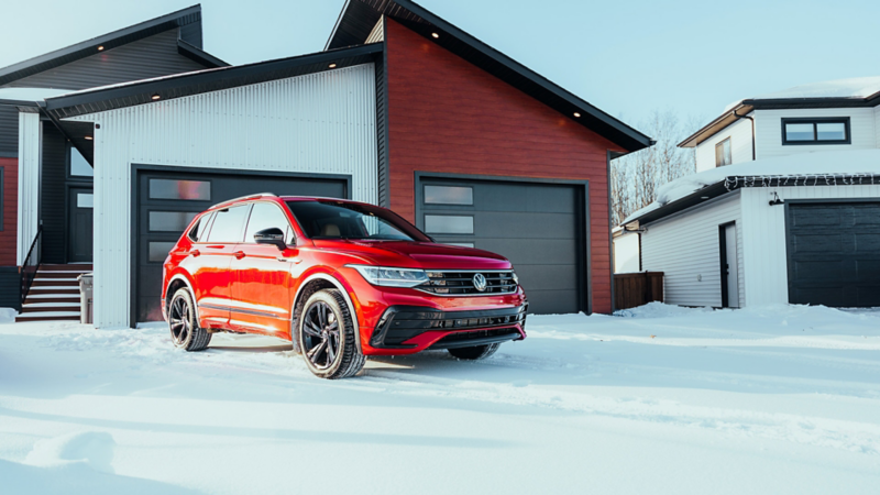 Un Volkswagen Tiguan R-Line rouge stationné dans une allée enneigée devant une maison moderne.