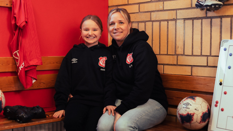 Fotbollstränare Cilla sitter på en bänk tillsammans med fotbollsspelaren Astrid