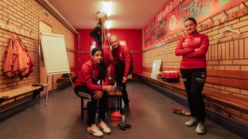 3 fotbollstjejer från FKIK står vid bänkarna i omklädningsrummet