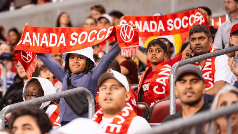 Foule au stade brandissant des écharpes rouges « CANADA SOCCER » avec le logo Volkswagen.