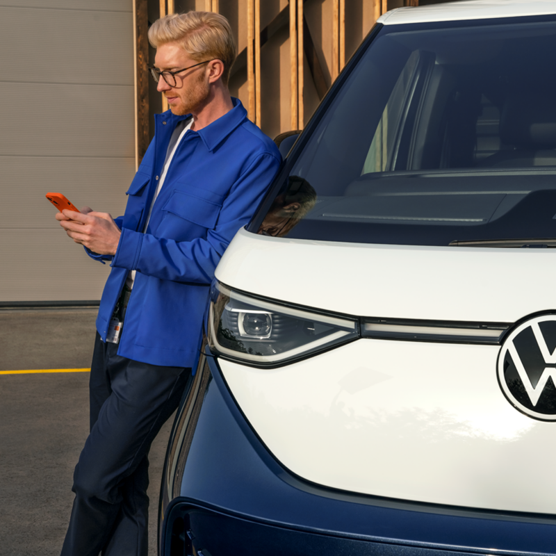 Un hombre usando el teléfono móvil, apoyado en el VW ID. Buzz.