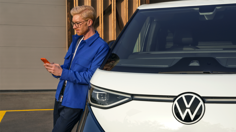 Un hombre usando el teléfono móvil, apoyado en el VW ID. Buzz.