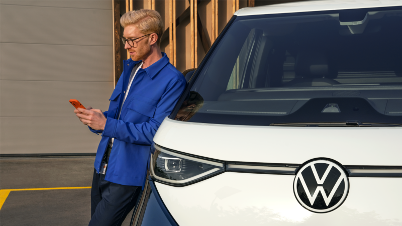 Un hombre usando el teléfono móvil, apoyado en el VW ID. Buzz.