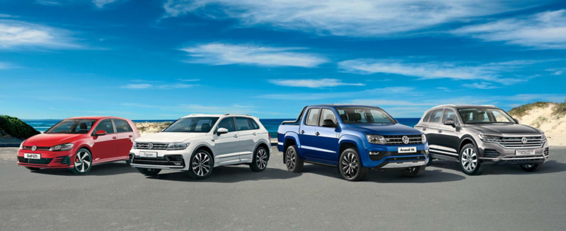 Volkswagen commercial vehicles, including a white van, a white truck, red sedan, and a blue SUV, parked together in an outdoor setting.