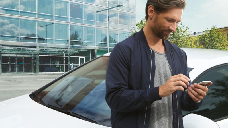 Besišypsantis žmogus vidiniame kieme su mobiliuoju telefonu rankoje priešais „Golf GTE“